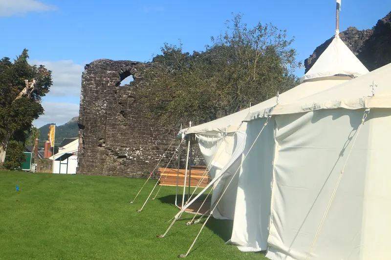 White marquees being put up on the lawn beside the ruined stone walls of Abergavenny Castle under a blue sky