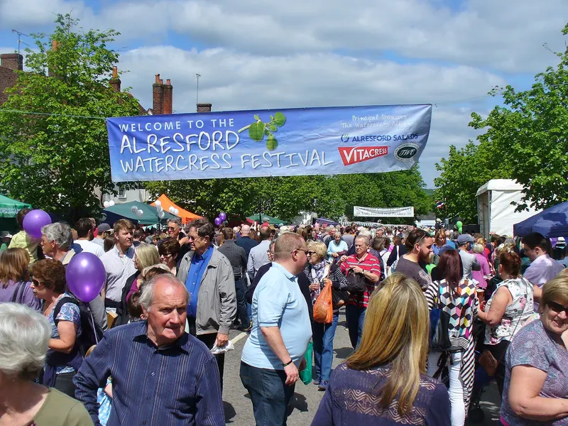 A dense crowd filling a town street beneath a 'Welcome to the Alresford Watercress Festival' banner