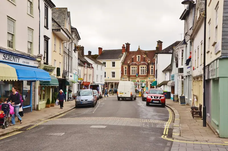 A narrow town street in Ashburton lined with shops and painted houses, leading to a brick building