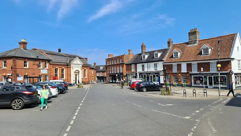 Aylsham's broad Market Place lined with Georgian brick buildings under a blue sky