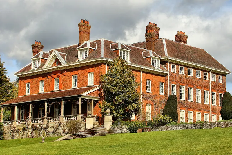 The red-brick Georgian house at Benington Lordship with a white veranda, beside lawns and trees