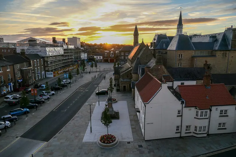 An elevated view along Bishop Auckland's Market Place at sunset, with stone buildings, a church spire and a golden sky