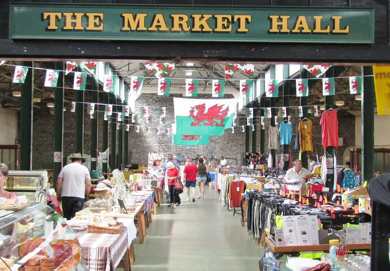 Stalls under strings of bunting and Welsh flags inside the Market Hall in Brecon, seen through its signed entrance