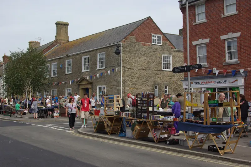 Shoppers browsing market stalls along South Street in Bridport, lined with stone and brick buildings