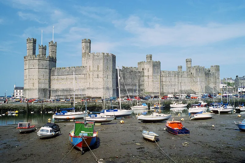 The towers and walls of Caernarfon Castle rising above small boats in the harbour under a blue sky