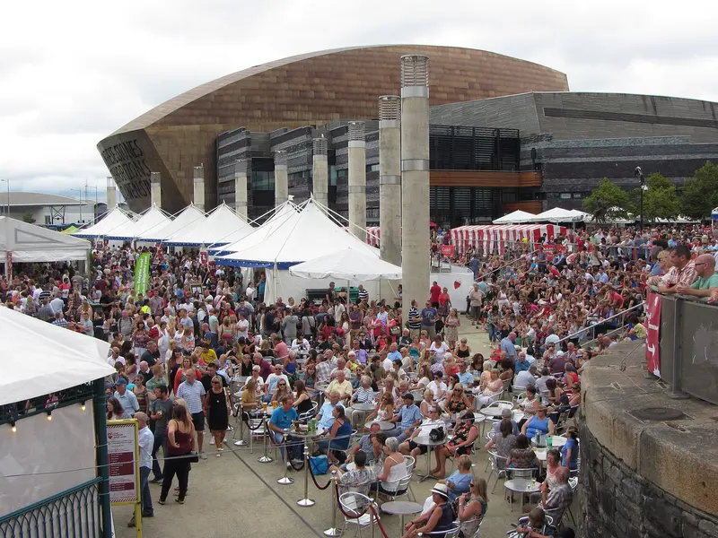 Crowds at tables among white festival marquees on Roald Dahl Plass, Cardiff Bay, with the Wales Millennium Centre behind