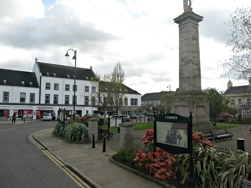The Square in Comber with its tall stone memorial column, flower beds and whitewashed buildings