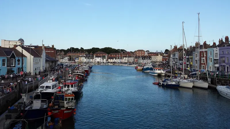 Weymouth's harbour lined with moored boats and colourful quayside buildings under a clear blue sky