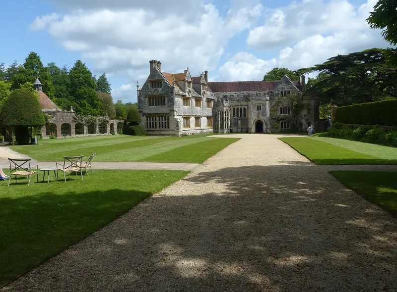 A gravel path leading across lawns to the stone Tudor manor house of Athelhampton, with walled gardens on either side