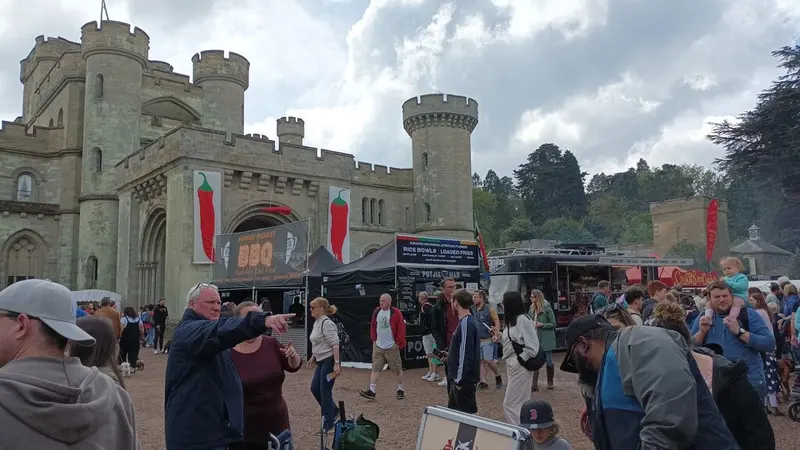 Crowds browsing street-food stalls in front of the turreted stone gatehouse of Eastnor Castle