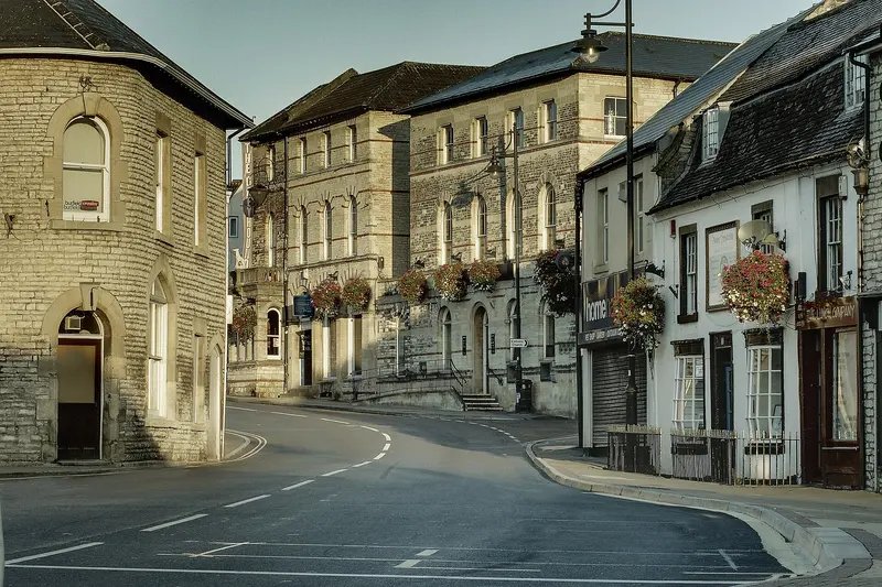 A quiet, curving High Street in Midsomer Norton lined with Victorian stone buildings and hanging flower baskets in low sunlight