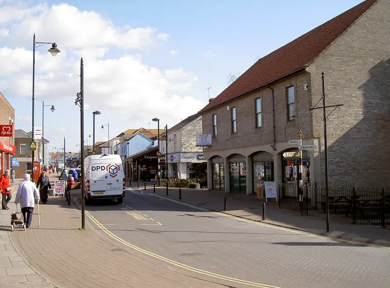Nailsea's High Street with shops, street lamps and pedestrians under a partly cloudy sky