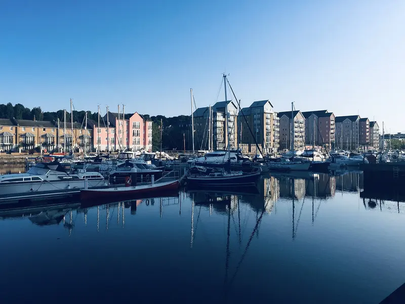 Yachts moored in Portishead Marina in front of modern waterside apartments, reflected in calm water under a blue sky
