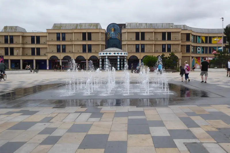 Ground-level fountains playing in a paved square in front of a modern colonnaded building