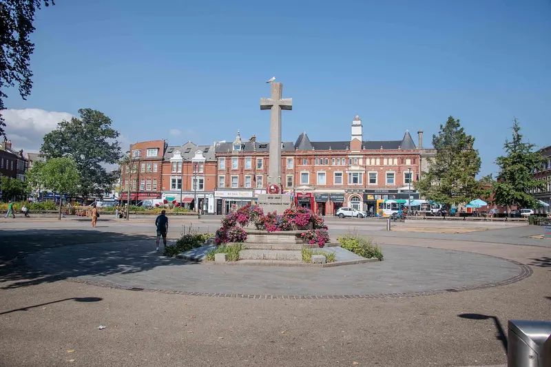 The Strand gardens in Exmouth town centre with a stone war memorial cross, flower beds and red-brick buildings under a blue sky