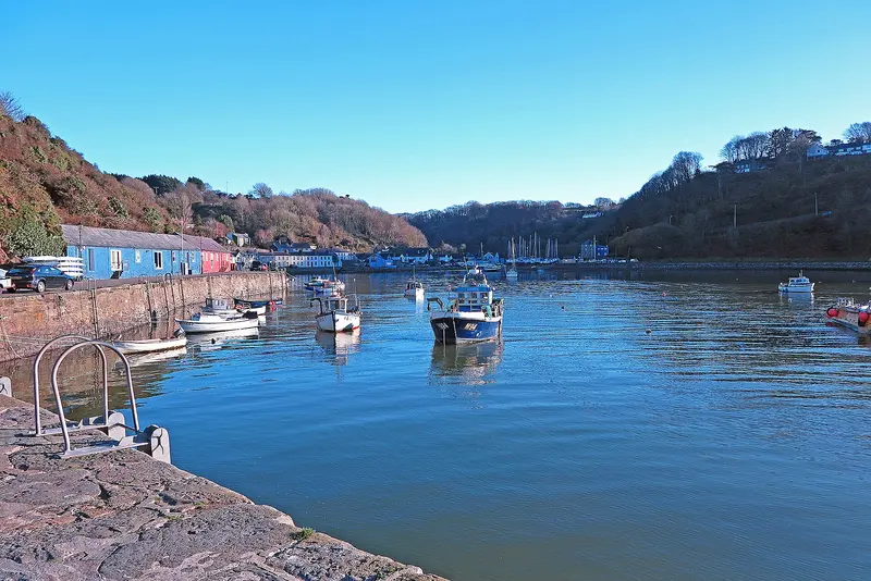 Small boats moored on calm blue water in the wooded inlet of Lower Fishguard harbour