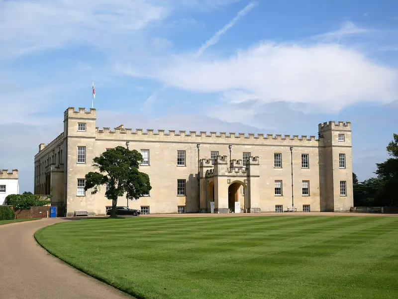 The castellated stone front of Syon House beyond a neatly striped lawn under a blue sky