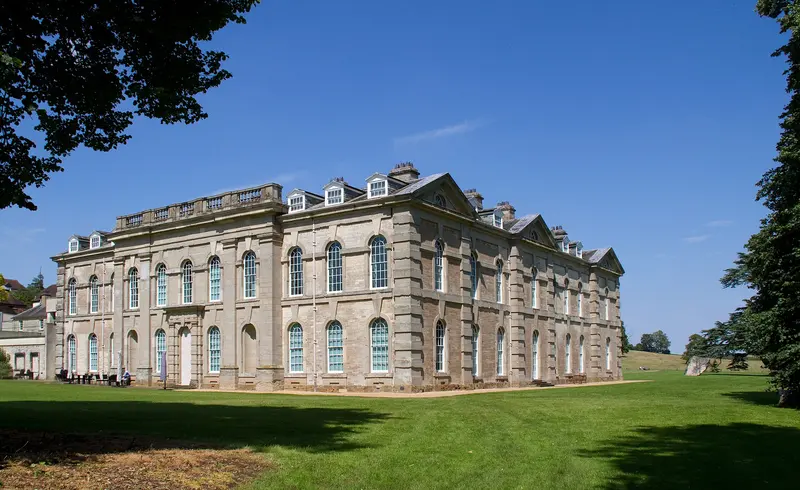 The long pale stone front of Compton Verney house on a lawn under a deep blue sky