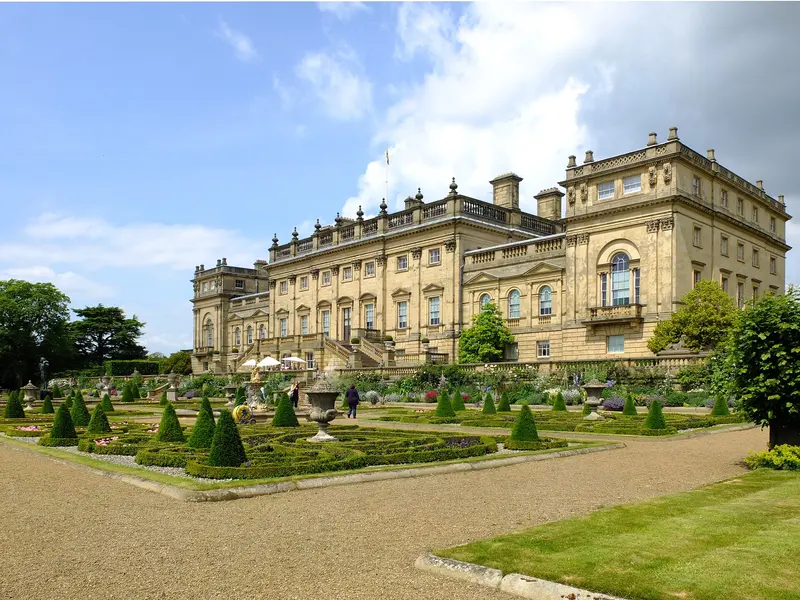 The long classical stone front of Harewood House seen across its formal terrace garden under a blue sky