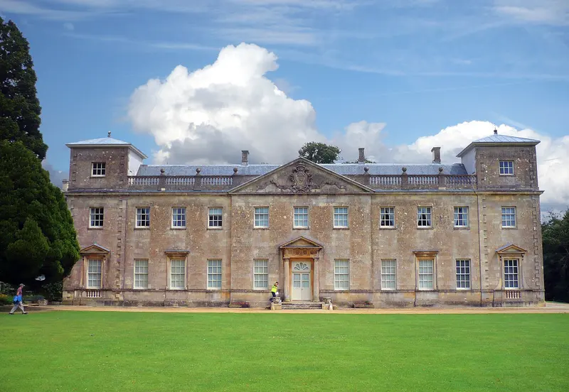 The Palladian front of Lydiard House beyond a mown lawn, framed by trees under a blue sky