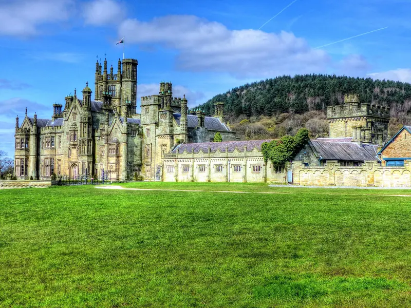 The towered Tudor Gothic front of Margam Castle above a sunny lawn, with wooded hills behind