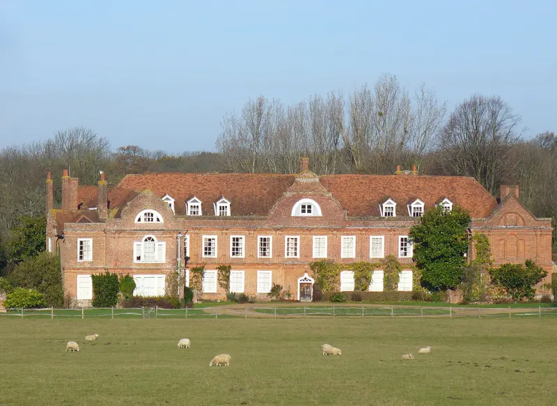 The long red-brick front of West Horsley Place seen across a sheep-grazed meadow