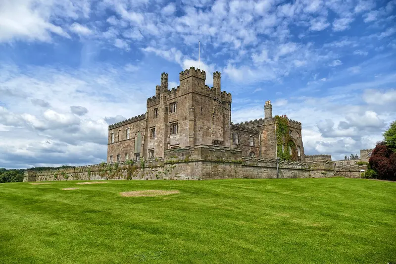 The battlemented stone front of Ripley Castle beyond a broad green lawn under a blue sky with white clouds