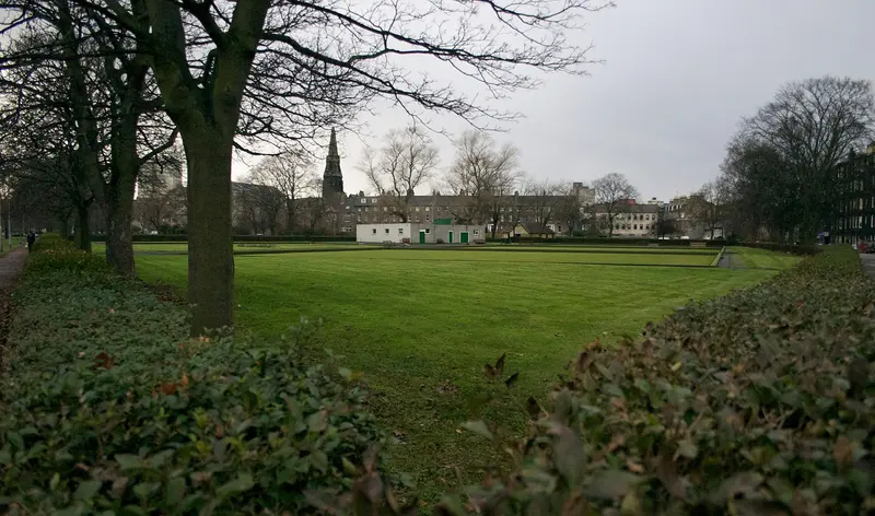 The open grass of Leith Links lined with tall trees, with a church spire beyond