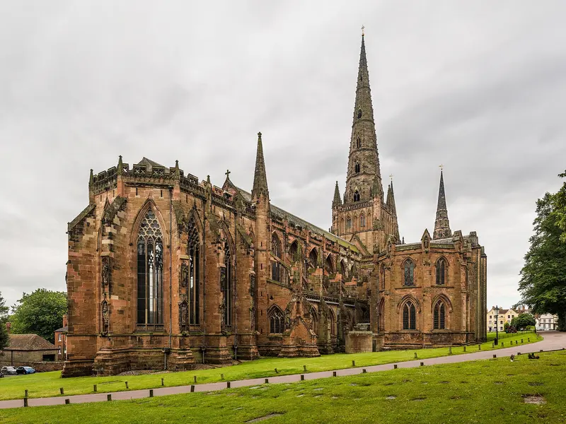 The red sandstone Lichfield Cathedral with its three spires, seen across a lawn