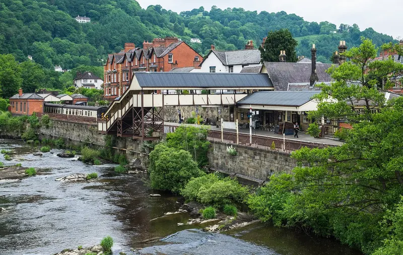 Llangollen's riverside railway station and town buildings above the rocky River Dee, with wooded hills behind