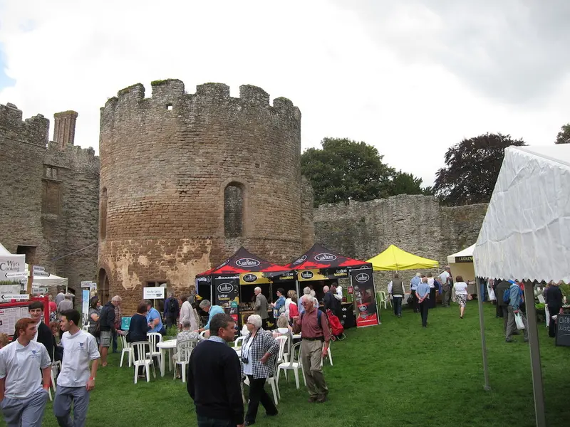 Visitors and food stalls on the lawn inside Ludlow Castle, with the round stone tower and castle walls behind