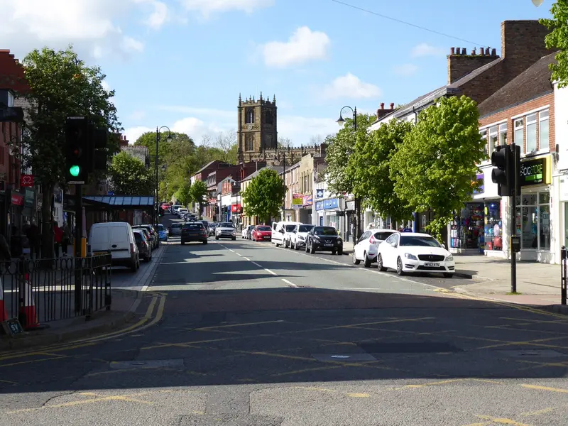Mold's wide High Street lined with shops and trees, leading up to the tower of St Mary's Church