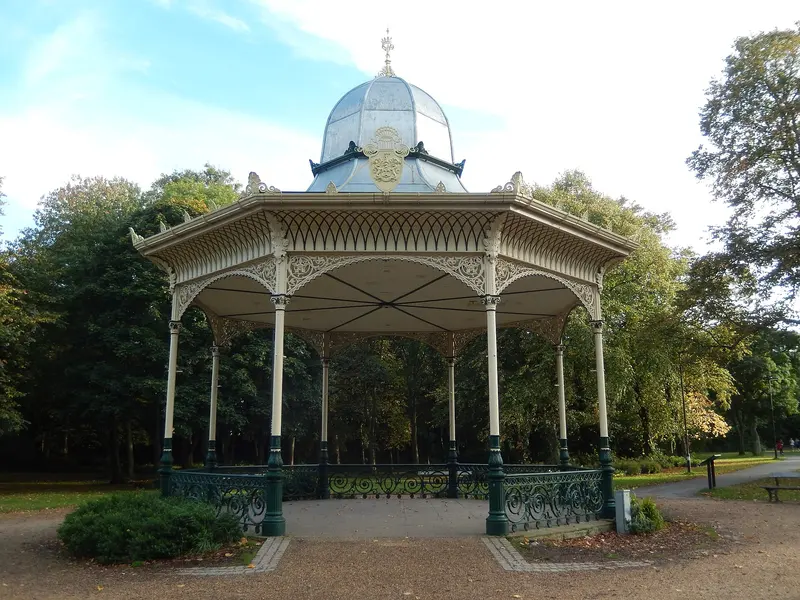 A restored Victorian bandstand with a domed roof among trees and flower beds in Exhibition Park