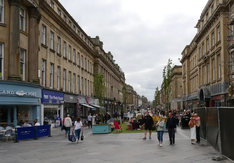 Shoppers walking along Grainger Street in Newcastle, lined with grand stone Victorian buildings
