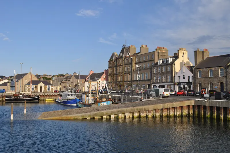 Kirkwall's harbour front with stone buildings and moored boats under a blue sky