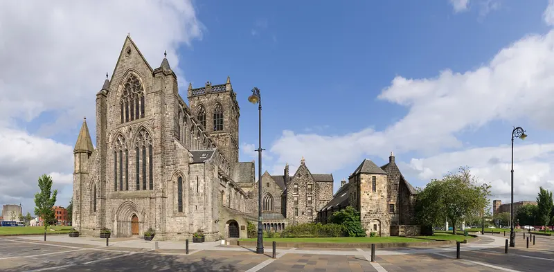 The Gothic stone west front of Paisley Abbey beside a square and street lamps under a blue sky