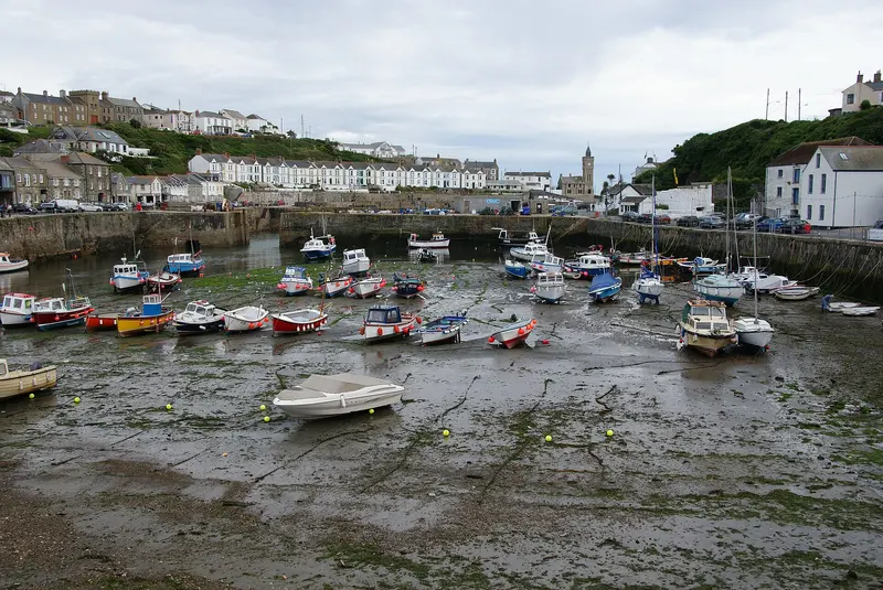 Boats resting at low tide in Porthleven's inner harbour, with houses and the clock tower around the harbour