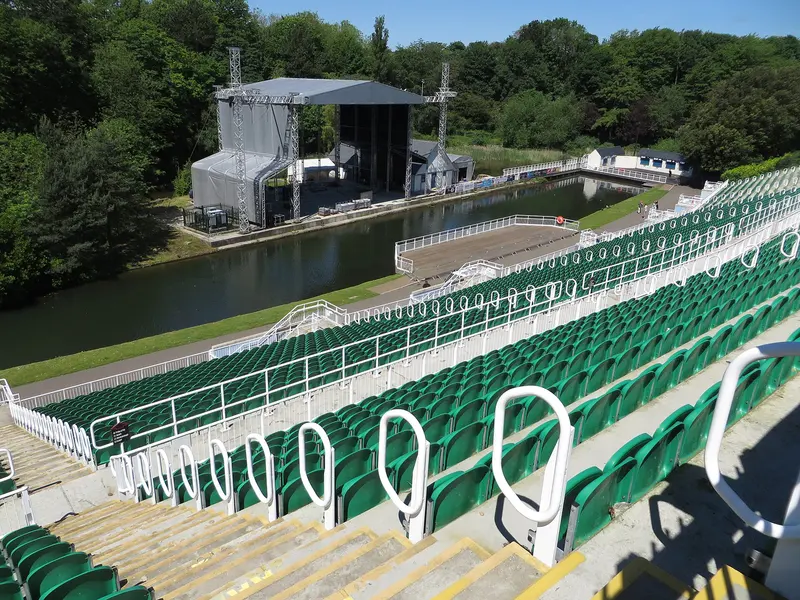 Tiers of green seating at Scarborough Open Air Theatre looking across a lake to the stage, surrounded by trees