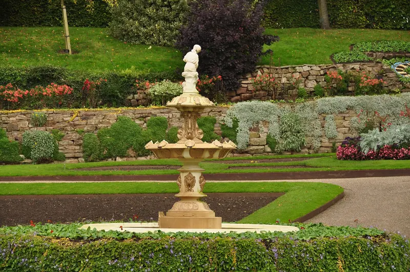 A white ornamental fountain surrounded by colourful flower beds in the Dingle garden