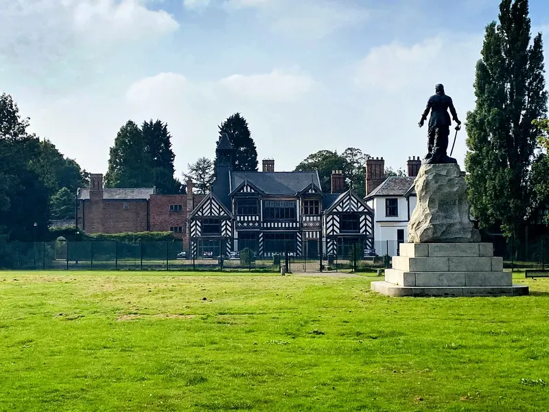 The black-and-white timber-framed Wythenshawe Hall beyond a lawn, with a statue of Oliver Cromwell on a plinth