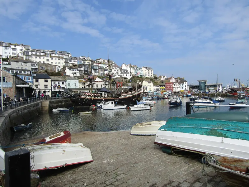 Boats in Brixham harbour beside a slipway, with colourful hillside houses rising behind