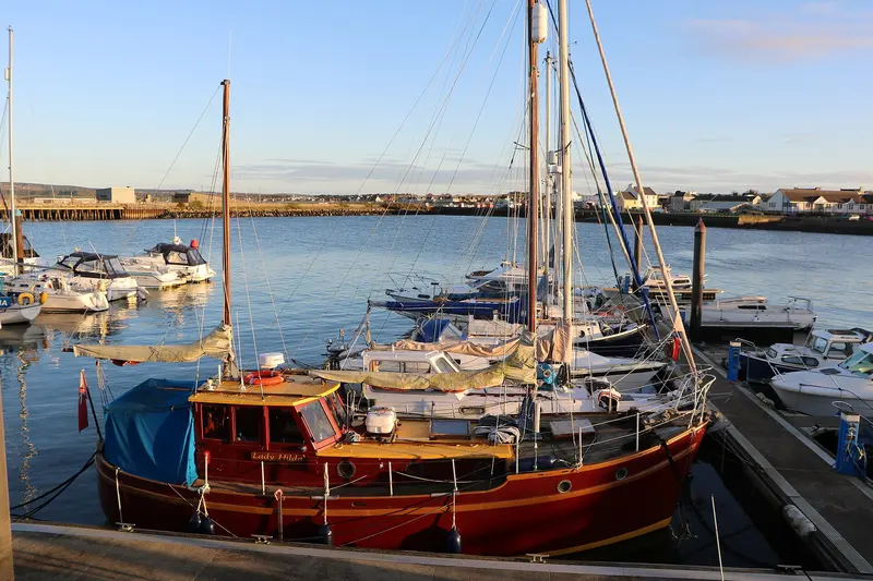 A wooden sailing boat and yachts moored in Stranraer Marina in low winter sunlight