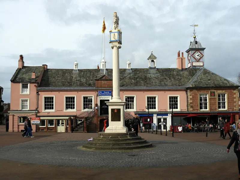 Carlisle's Market Cross column and the pink-rendered Old Town Hall with its clock cupola, on a wide paved square