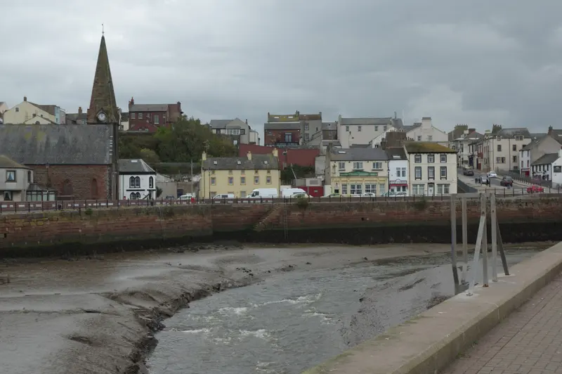 Maryport's harbour channel at low tide, with the town's houses and a church spire beyond