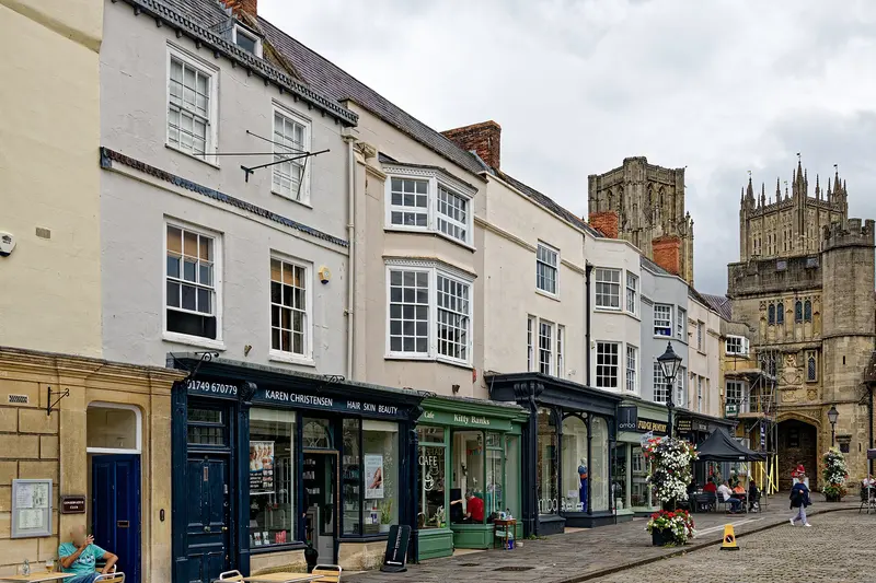A row of historic shopfronts on Wells Market Place, with the towers of Wells Cathedral rising behind