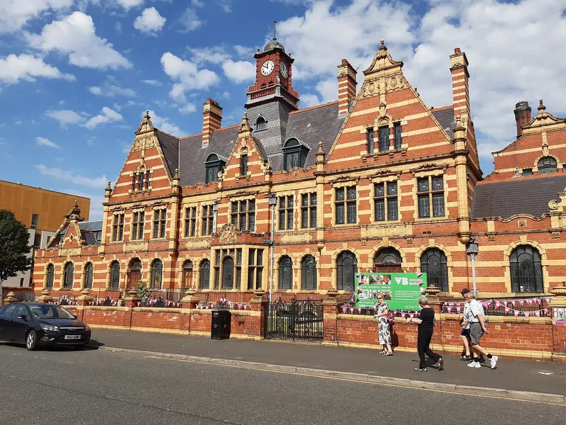 The ornate red-brick and terracotta Edwardian frontage of Victoria Baths in Manchester under a blue sky