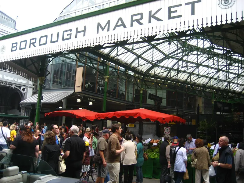 Crowds of shoppers beneath the green ironwork entrance sign of Borough Market in London