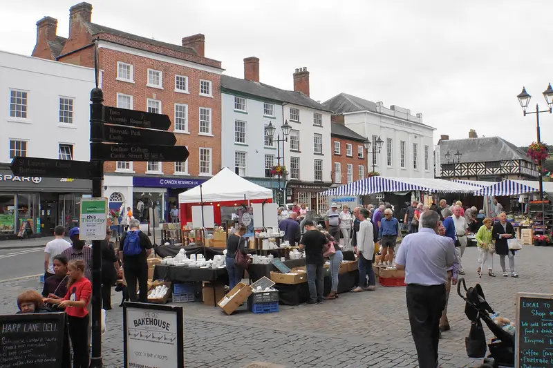 Shoppers browsing market stalls in Ludlow's Castle Square, lined with Georgian buildings